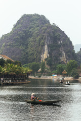 Landscape of mountain and river with Vietnamese woman rowing boat by her feet at Trang An Grottoes in Ninh Binh, Vietnam.