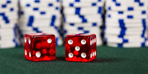 Dice on a poker table with gambling poker chips stacked behind representing a win at a casino.