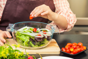 Female cook making fresh salad in her home cooking, various vegetables on table