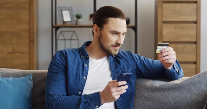 Handsome caucasian man holding a smartphone and entering the number of the credit card while shopping online. Inside