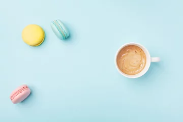 Keuken spatwand met foto Cozy morning breakfast. Cup of coffee and colorful macaron on pastel blue background top view. Fashion flat lay style. Sweet macaroons. © juliasudnitskaya