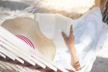 Young lady reading a book in hammock on tropical sandy beach.