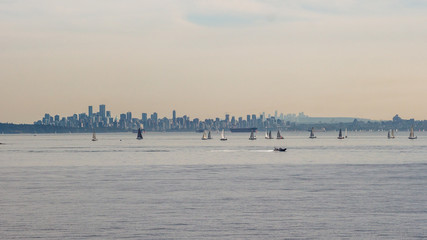 Plenty of yachts on the ocean in front of the big high rise modern city far away in the horizon