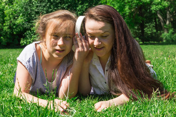 Two girls spending time together in city park. Listen music by smart phone.