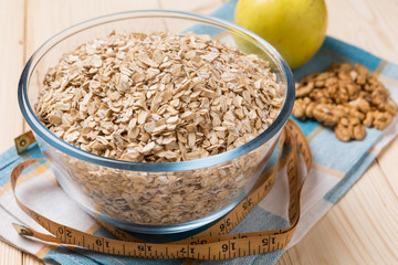 oat flakes in a glass plate, nuts and apples on a wooden board, concept of a healthy lifestyle