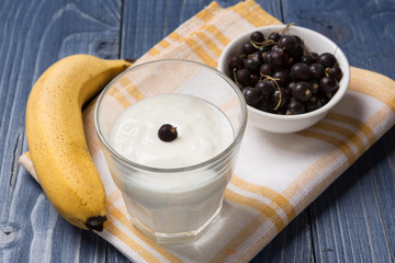 yogurt in a glass, banana and currant on wooden boards