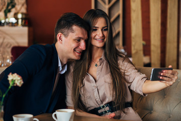 Joyful loving couple enjoying modern technology, having fun, capturing bright moments of vacations in cafe