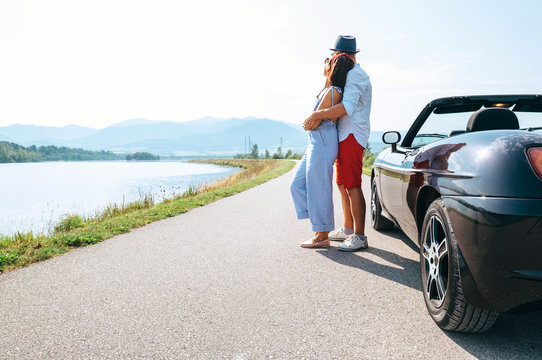 Couple in love stands near the cabriolet car on the picturesque mountain road