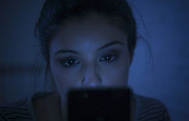 portrait of young beautiful latin woman using mobile phone late night sleepless lying in bed in the dark in smartphone and internet dating app addiction