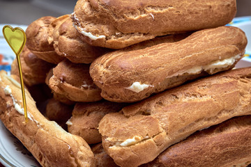 On the plate there are several home-made eclairs. Eclairs cut in half. Stuffed with vanilla butter cream. Handmade cakes. Sweets for a birthday or a holiday. Cakes are stacked in a pile.
