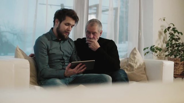 Hipster son and his senior father with tablet at home.