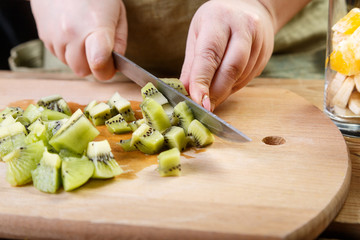 A woman cuts into small pieces of a kiwi knife on a wooden board. Close-up, horizontal frame