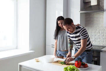 Smiling young couple cooking healthy food in the white home kitchen together