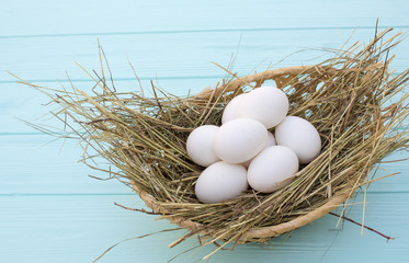 chicken eggs in a basket with hay on a turquoise wooden background. eggs on the hay