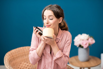 Young woman enjoying aroma of a body lotion sitting on the blue wall background at home