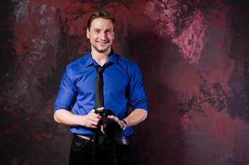 Studio portrait of stylish professional photographer man with camera, wear on blue shirt and necktie.