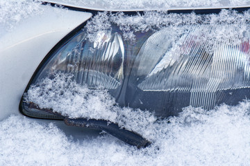 Close up of a car headlight with the wiper partly under the snow