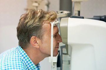 health care, medicine, people, eyesight and technology concept - man checks his vision on the machine checking patient vision at eye clinic or optics store. face close-up