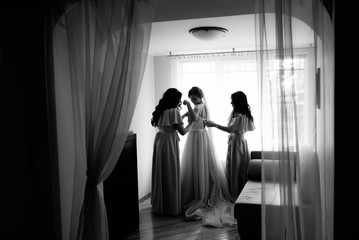 A bride getting dressed for the wedding and being helped by her bidesmaid in a dark room.