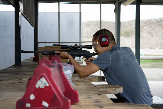 Asian man shooting rifle at shooting range