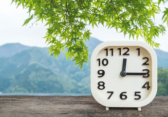 Closeup white clock for decorate show a quarter past twelve o'clock or 12:15 p.m. on blurred mountain view background