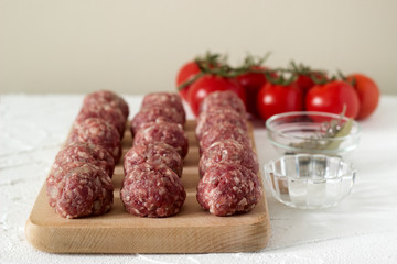 Raw meatballs, tomatoes and spices on a white concrete background. Rustic style.