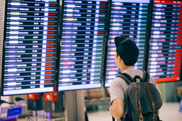 Young male traveler watching and waiting for flight time schedule on boarding time monitor screen