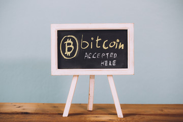 Virtual currency Bitcoin accepted here sign on wooden platform over pastel blue background