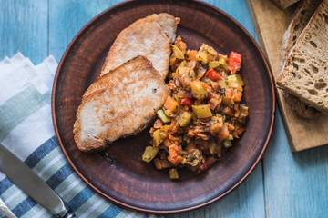 Vegetable stew and pieces of fried meat in a plate on a wooden rustic background with sliced bread - top view