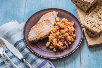 Vegetable stew and pieces of fried meat in a plate on a wooden rustic background with sliced bread - top view