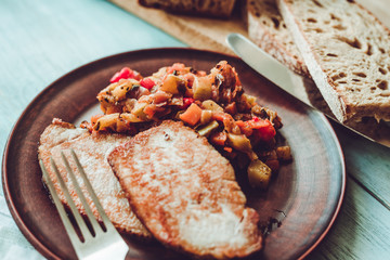 Vegetable stew and pieces of fried meat in a plate on a wooden rustic background with sliced bread - close-up
