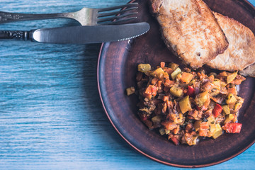 Vegetable stew and pieces of fried meat in a plate on a wooden rustic background with sliced bread - copy space for a recipe