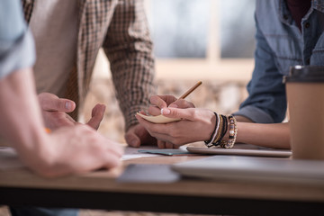 Not to forget. Nice positive young woman standing with her colleague and taking notes while working with him