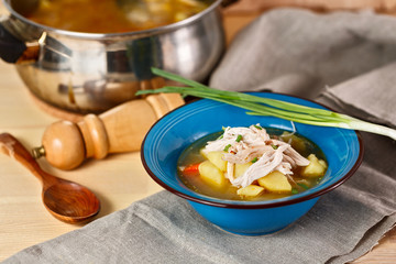 homemade chicken soup with vegetables in blue plate on wooden table.