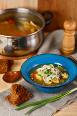 homemade chicken soup with vegetables in blue plate on wooden table.