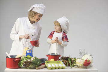 Mother teaches son to cook on light background.