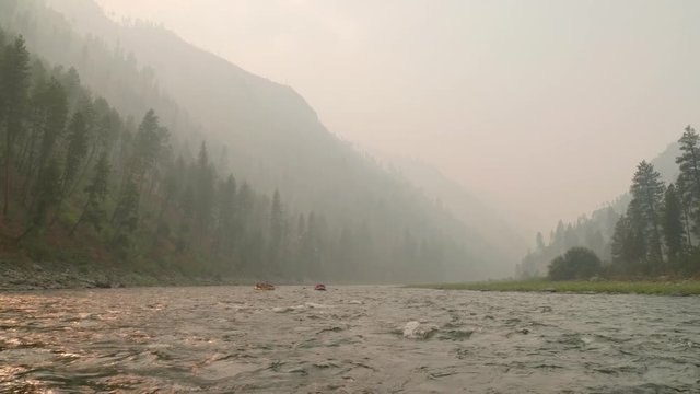 Rafts Floating Down A River Through Forrest Filled With Smoke From Fire