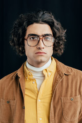 Portrait of male fashion model with curly hair in eyeglasses isolated on black