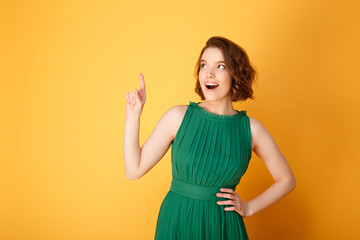 portrait of young emotional woman pointing up isolated on orange