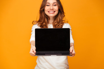 Smiling brunette woman in sweater showing blank laptop computer screen