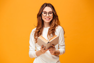 Smiling brunette woman in sweater and eyeglasses holding book - obrazy, fototapety, plakaty