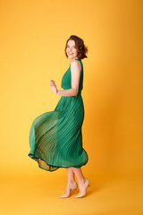 Fototapeta na wymiar dancing beautiful woman in green dress isolated on orange
