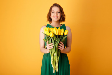 portrait of smiling woman holding bouquet of yellow tulips isolated on orange