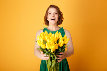 happy young woman holding bouquet of yellow tulips in hands isolated on orange