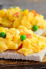 Delicious scrambled eggs with vegetables on crispy toast. Scrambled omelette toast recipe. Simple homemade cooking. Vertical photo. Closeup