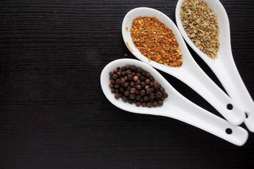 Black and red pepper, set of spices in spoons. On black wooden table