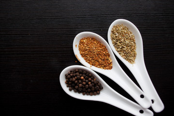 Black and red pepper, set of spices in spoons. On black wooden table
