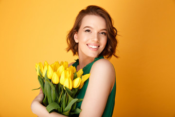 portrait of happy woman with bouquet of yellow tulips isolated on orange