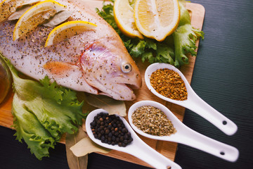 Fresh trout and ingredients to prepare fish dishes on black table