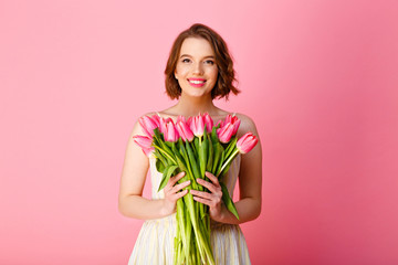portrait of smiling woman with bouquet of pink tulips in hands isolated on pink